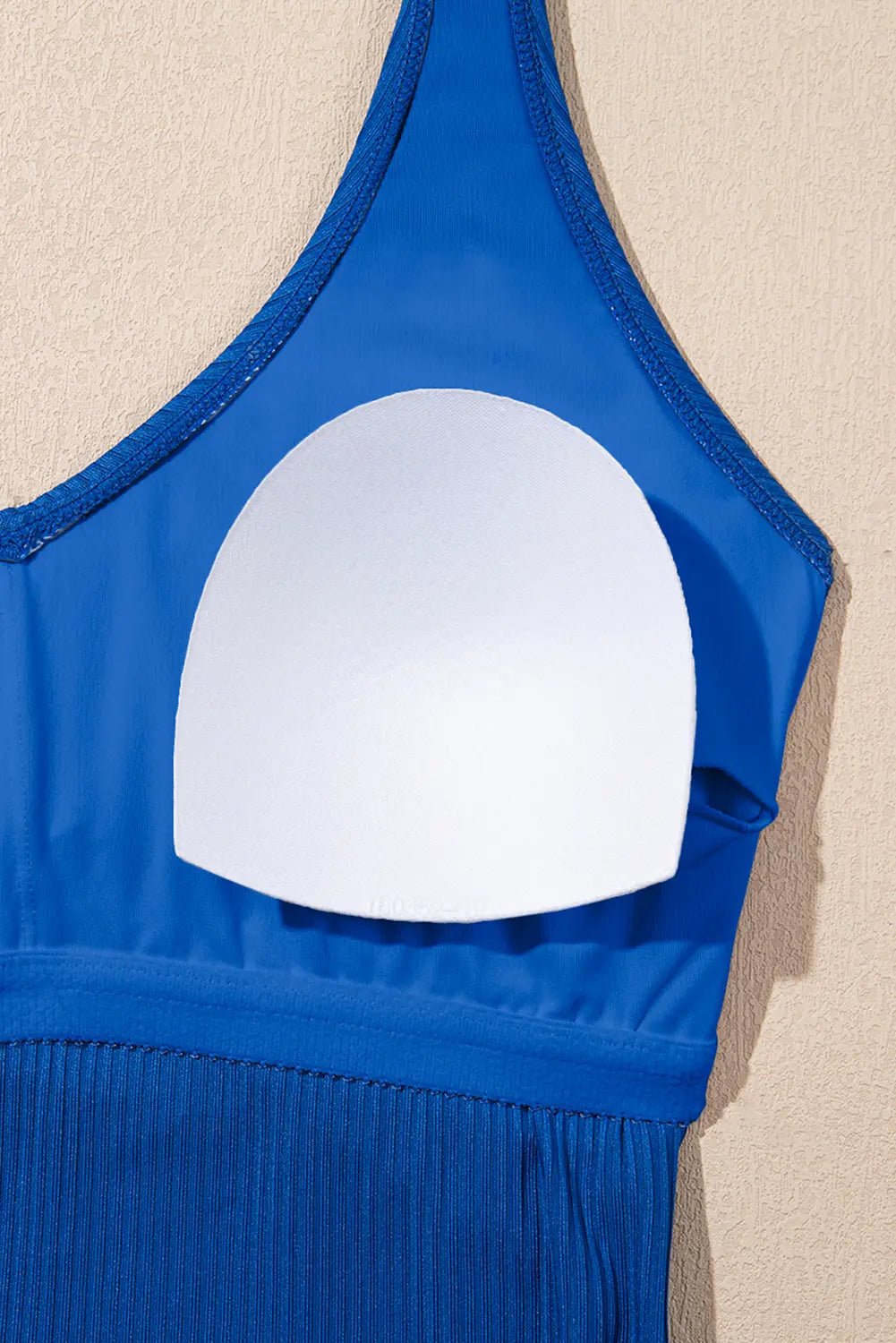 Blue swimsuit top with a white circular cutout on a beige background