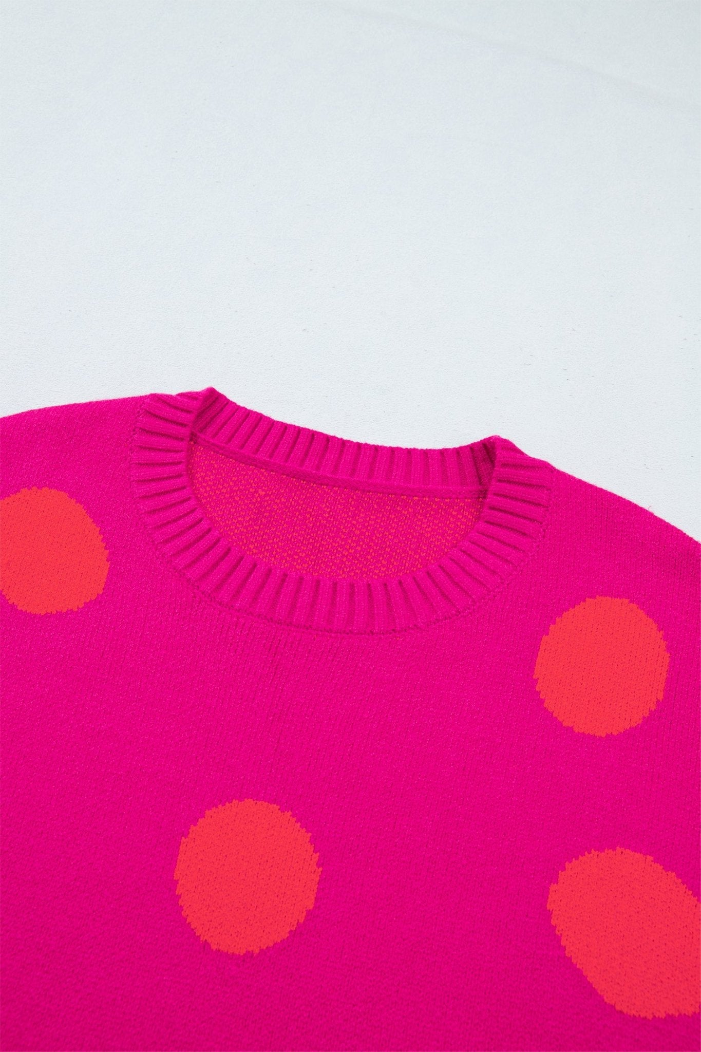 Close-up of bright pink knit sweater with orange-red dots.