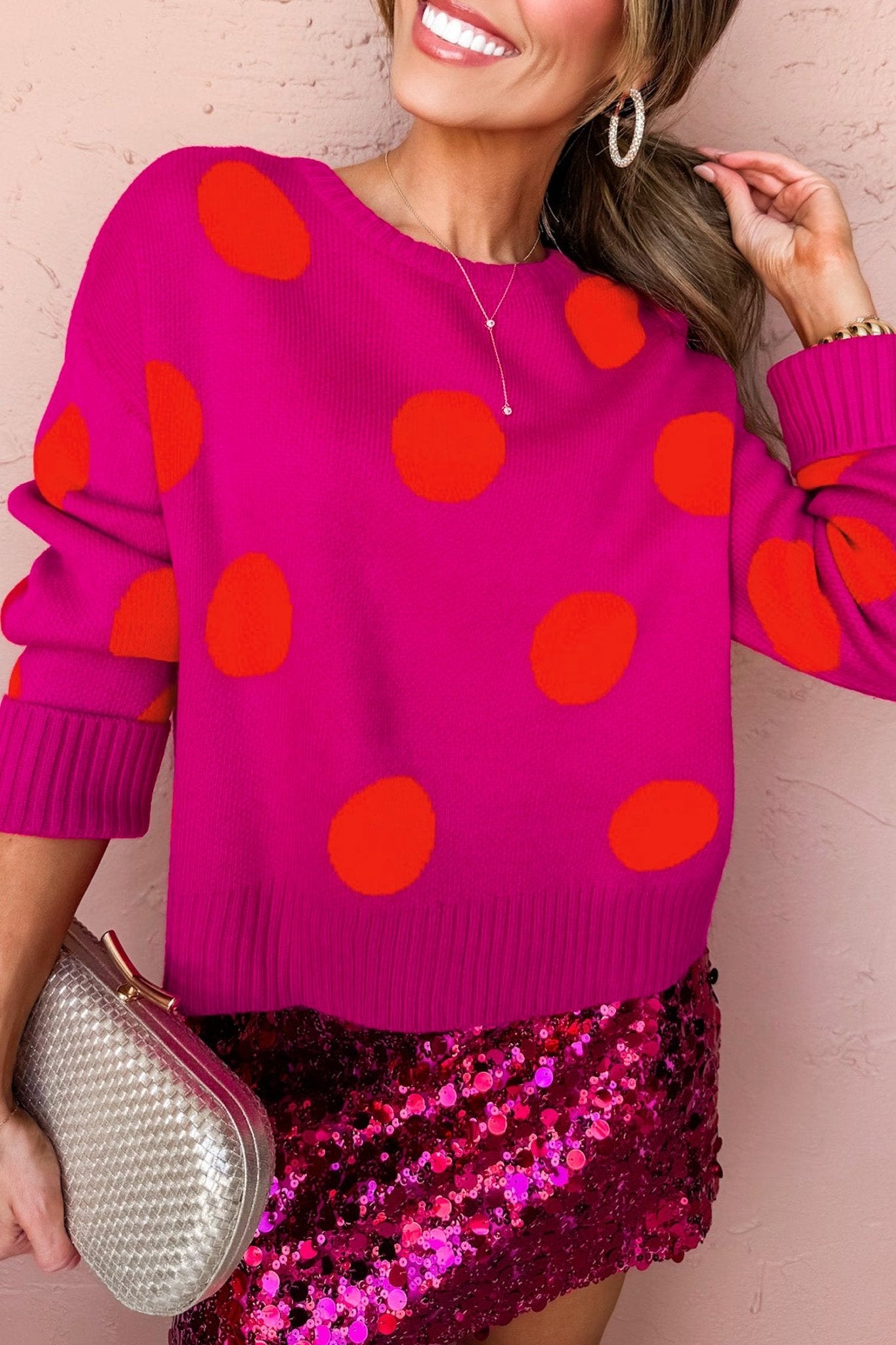 Woman in pink polka-dot sweater & sequined skirt with clutch.