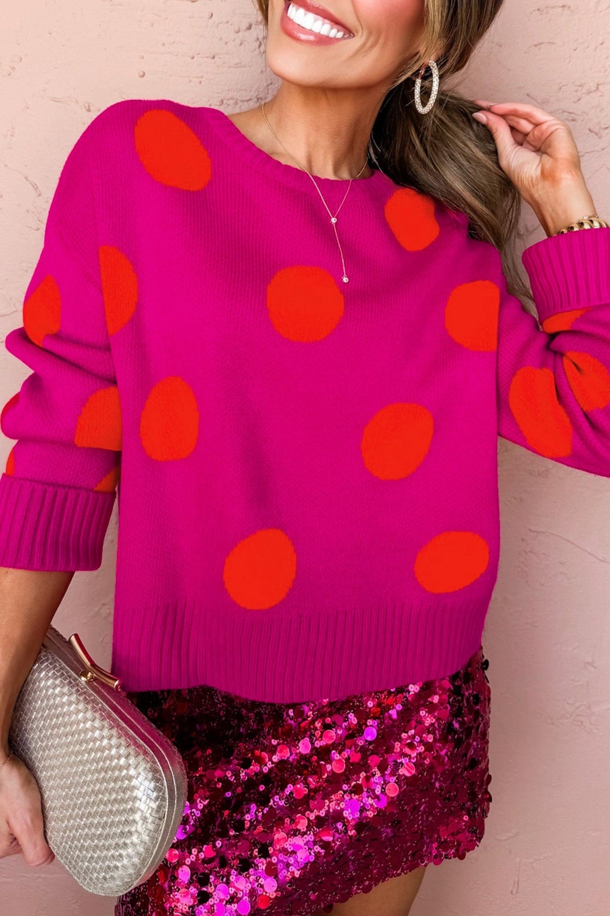 Woman in pink polka-dot sweater & sequined skirt with clutch.