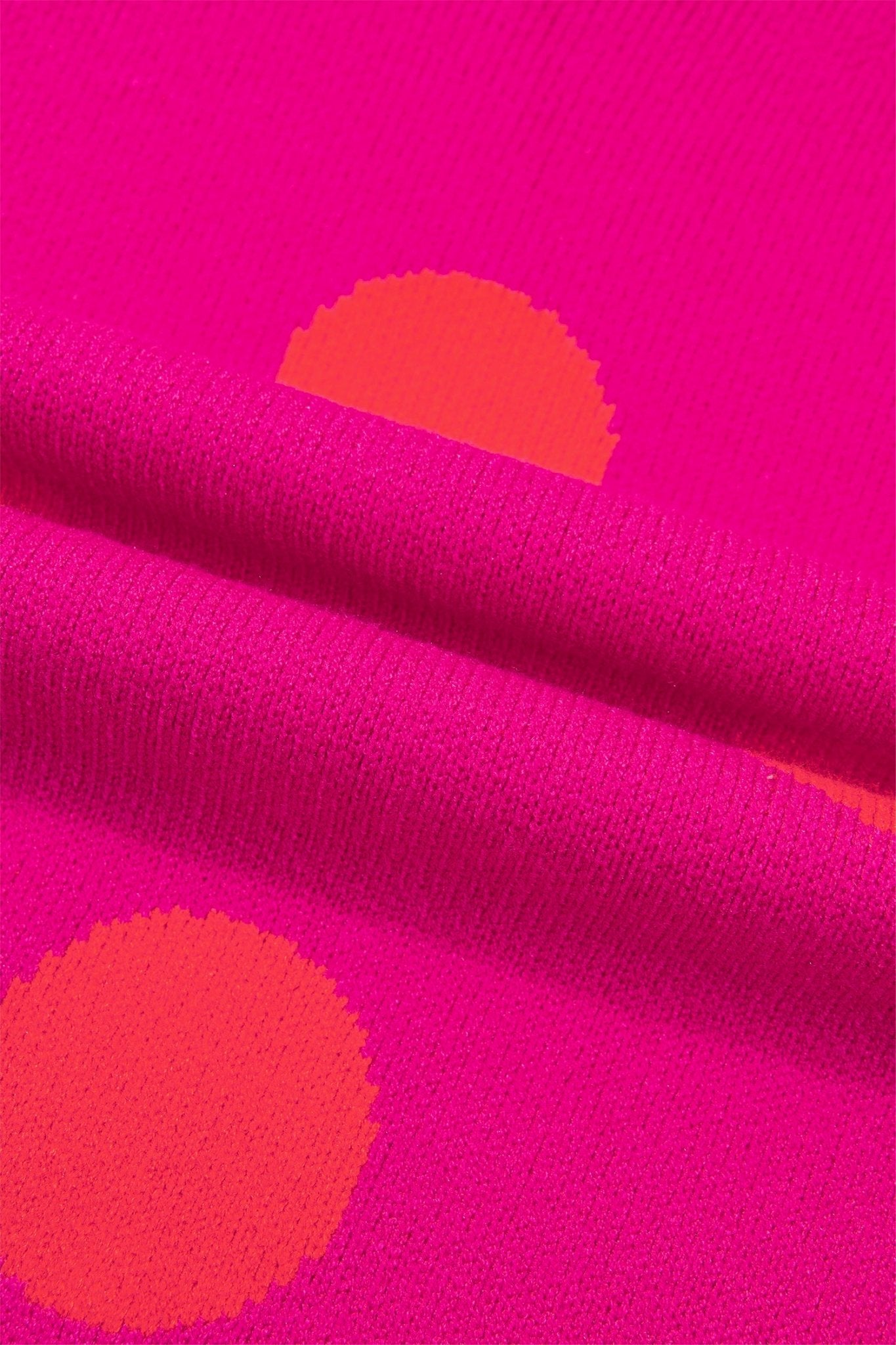 Bright pink knit fabric with large orange polka dots and a folded section showing the texture.