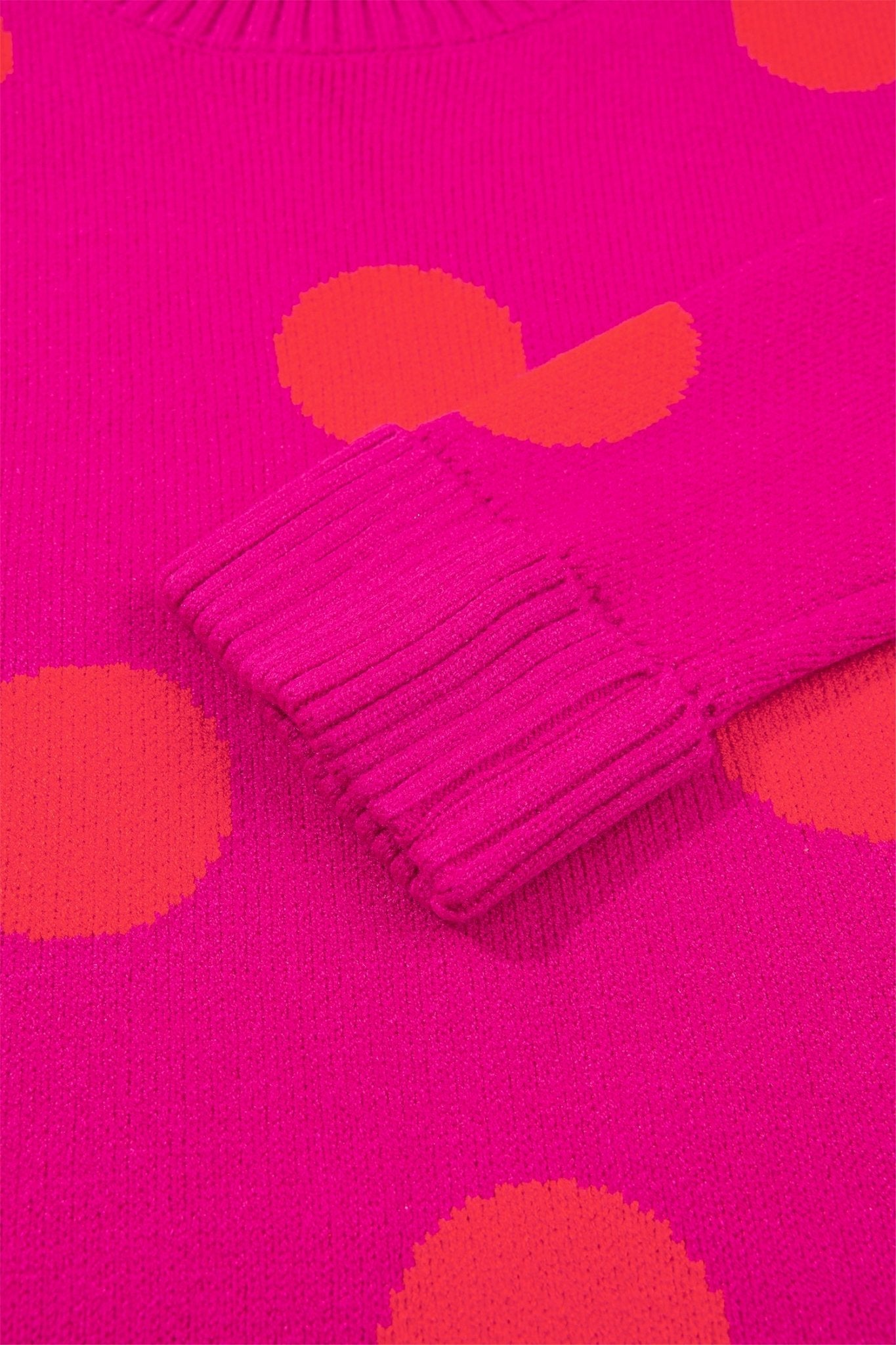 Close-up of bright pink ribbed knit fabric with orange dots on light gray textured surface.