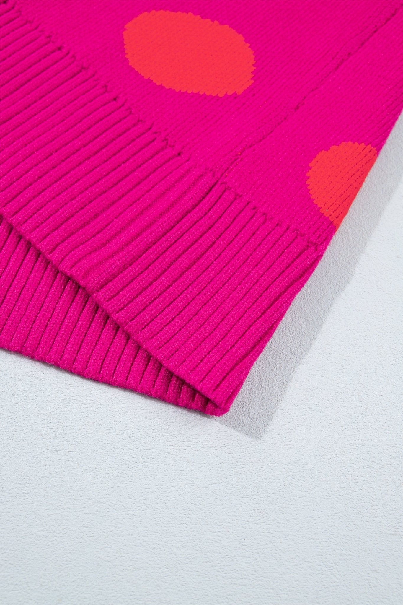 Close-up of bright pink ribbed knit fabric with orange dots on light gray textured surface.