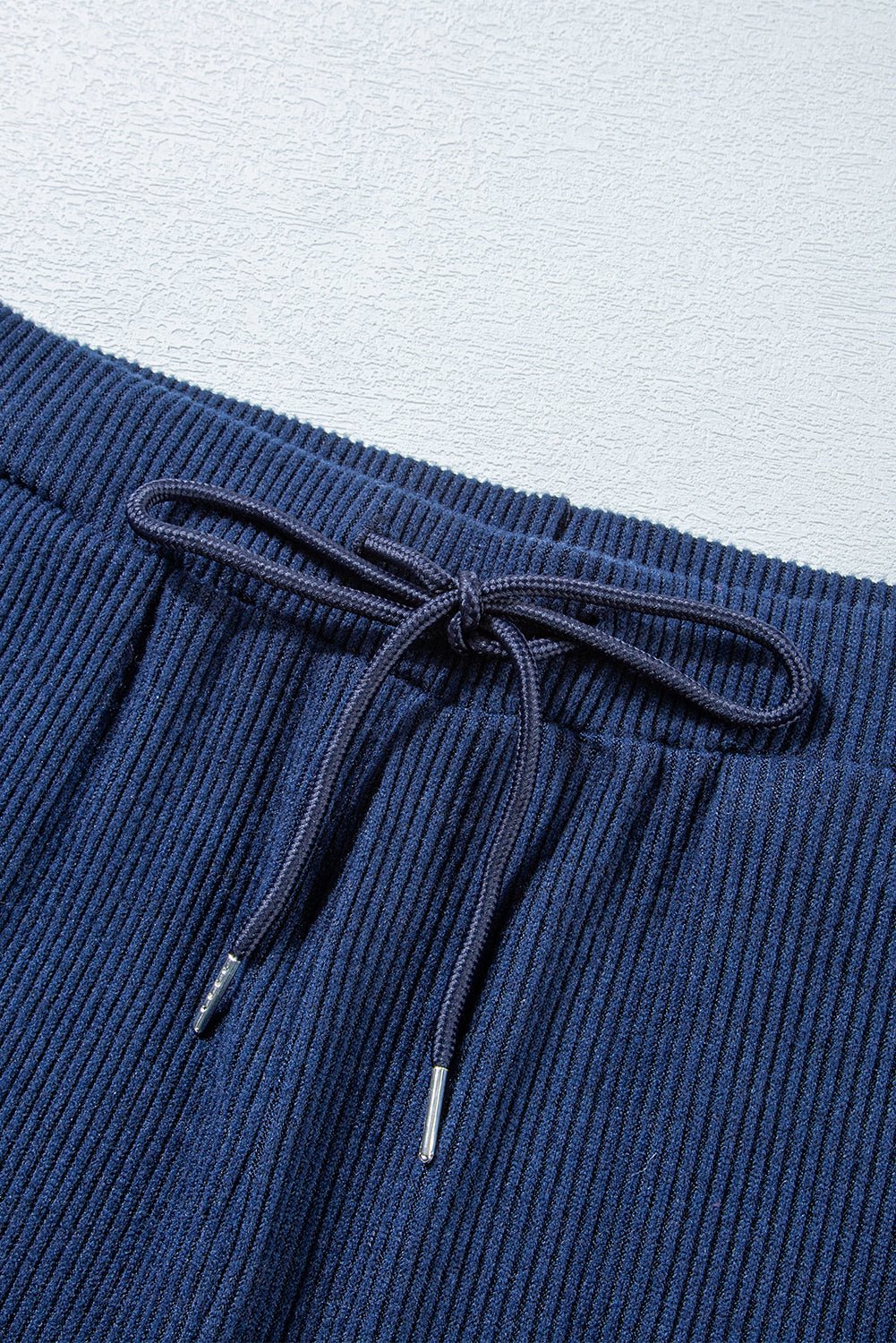 Close-up of blue ribbed knit pants with drawstring on a light gray background