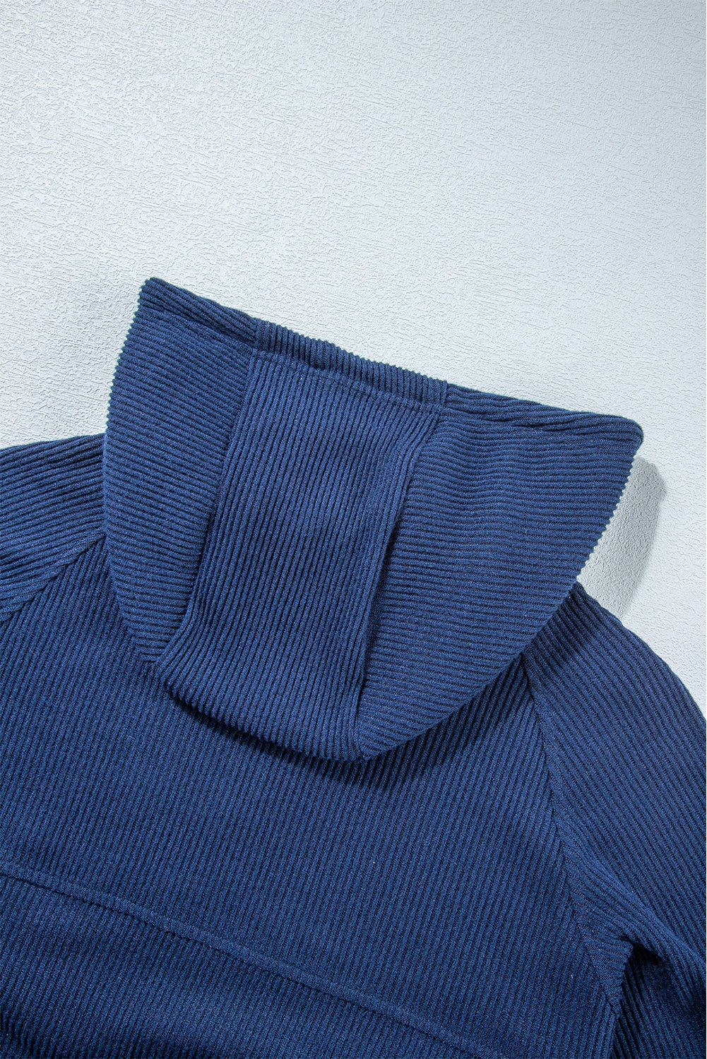 Close-up of a blue ribbed sweater with a hood on a light gray background