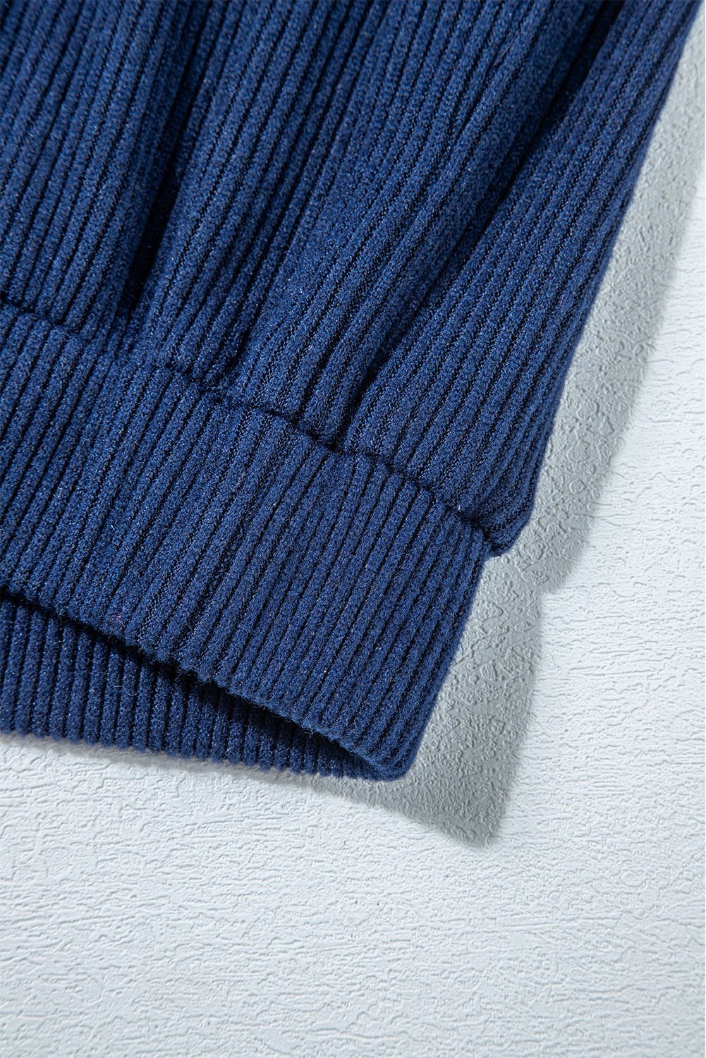Close-up of a blue ribbed sweater sleeve on a light gray background