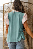 Person wearing a teal ribbed tank top and light pink sleeves, standing in front of a textured wall.