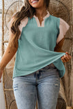 Woman wearing a green sleeveless top and jeans standing against a woven wall.