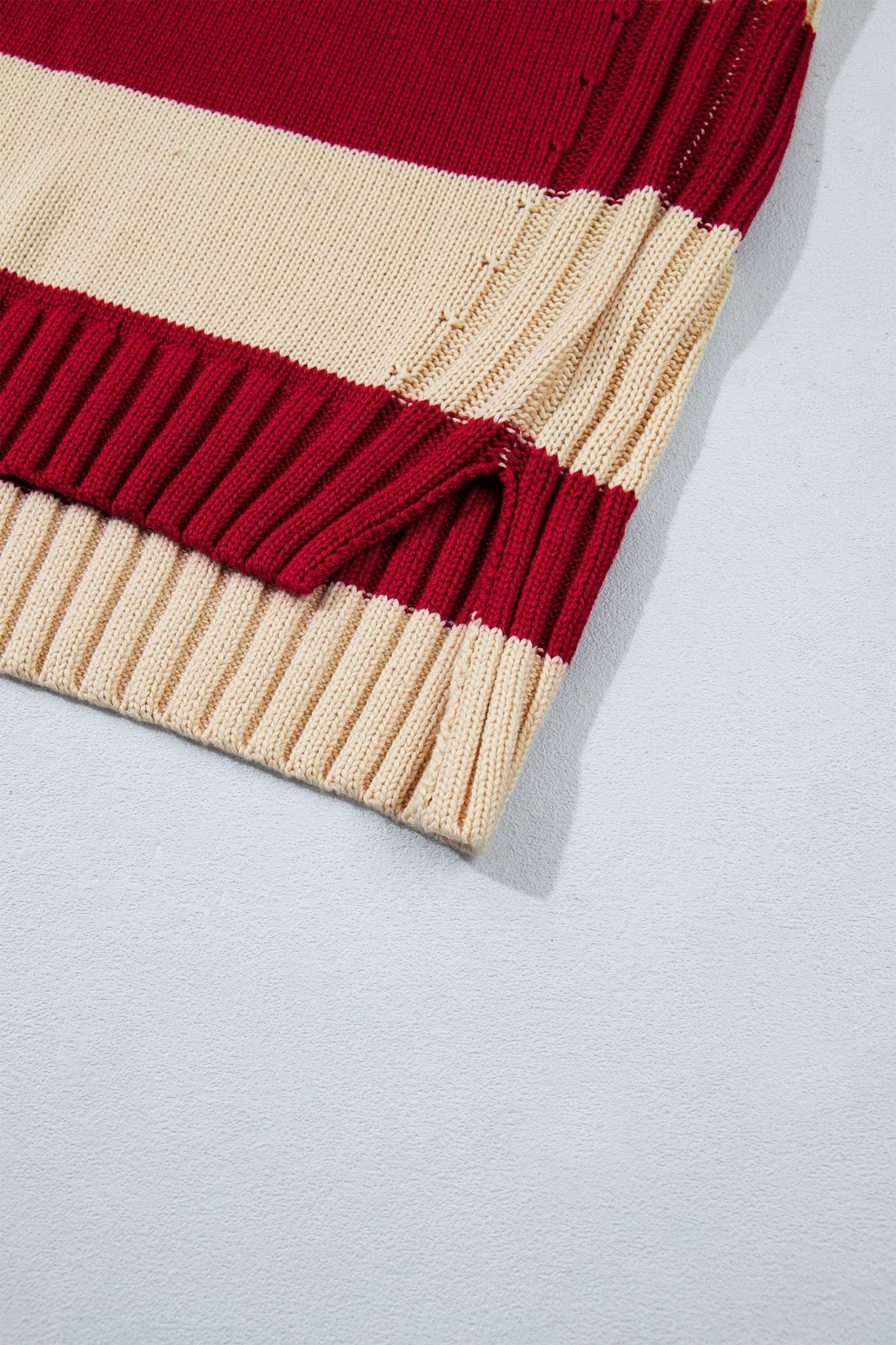Close-up of burgundy and cream striped ribbed knit sweater on gray background.
