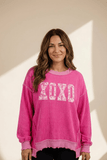 Woman wearing a pink 'XOXO' sweater against a neutral background