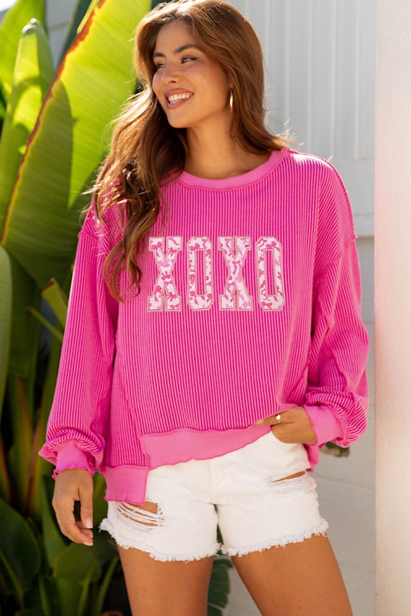 Woman wearing a pink sweatshirt with 'XOXO' text, standing outdoors.
