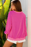 Woman wearing a bright pink ribbed sweater and white shorts standing next to a plant.