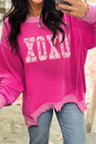 Person wearing a bright pink sweater with 'XOXO' print, taking a mirror selfie.