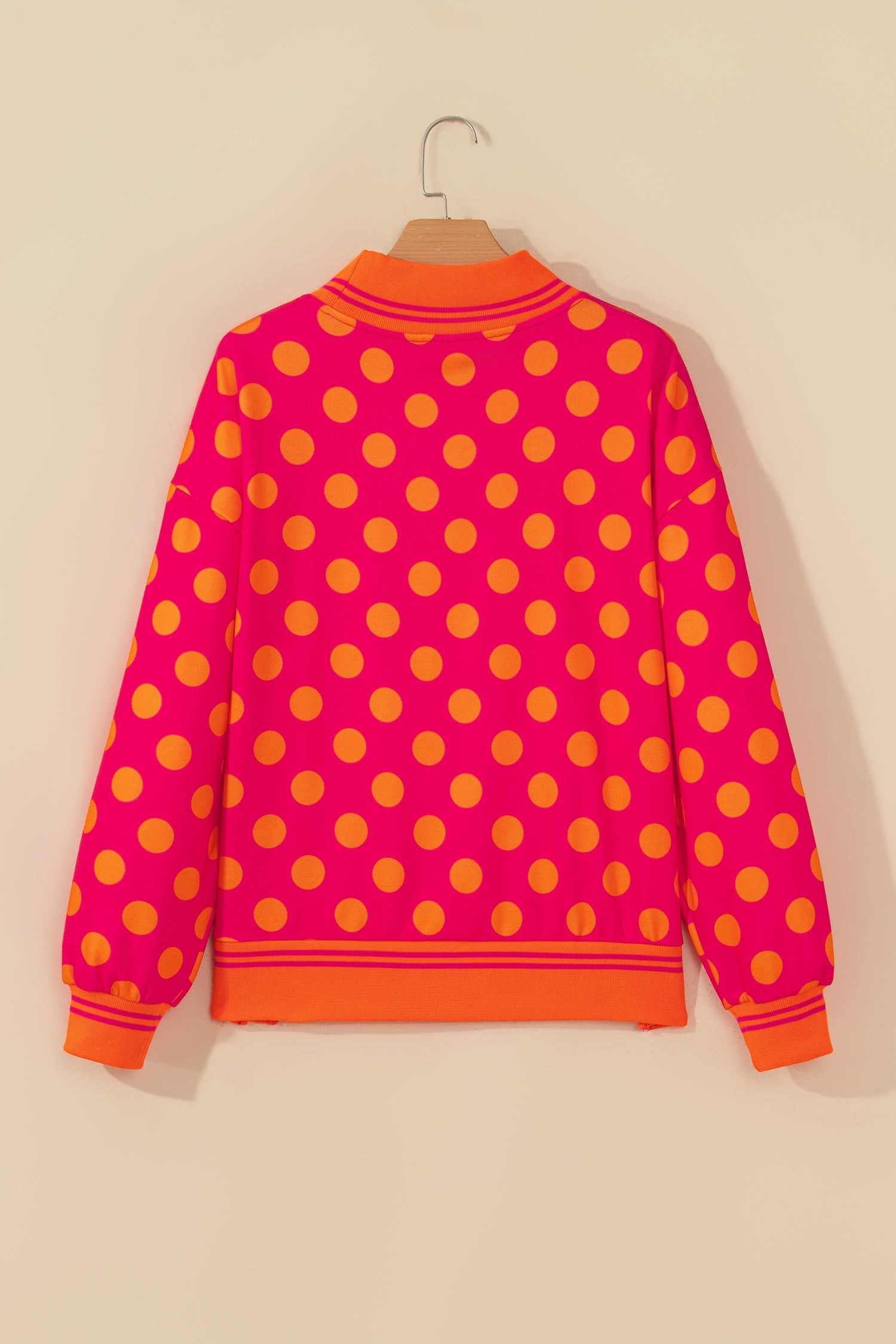 Rose polka dot sweatshirt with orange striped cuffs and hem on a hanger