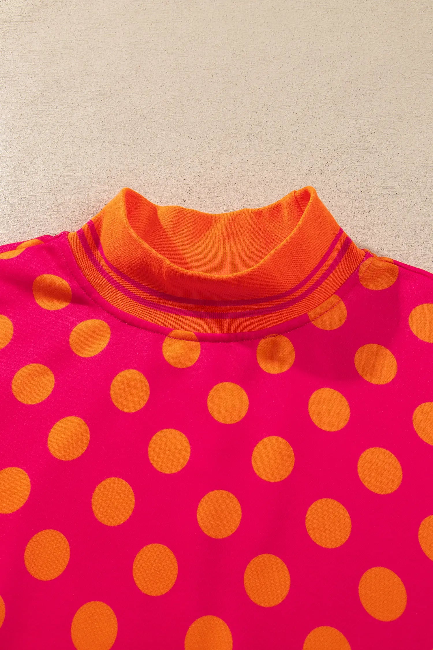 Close-up of orange striped mock neck on rose polka dot sweatshirt