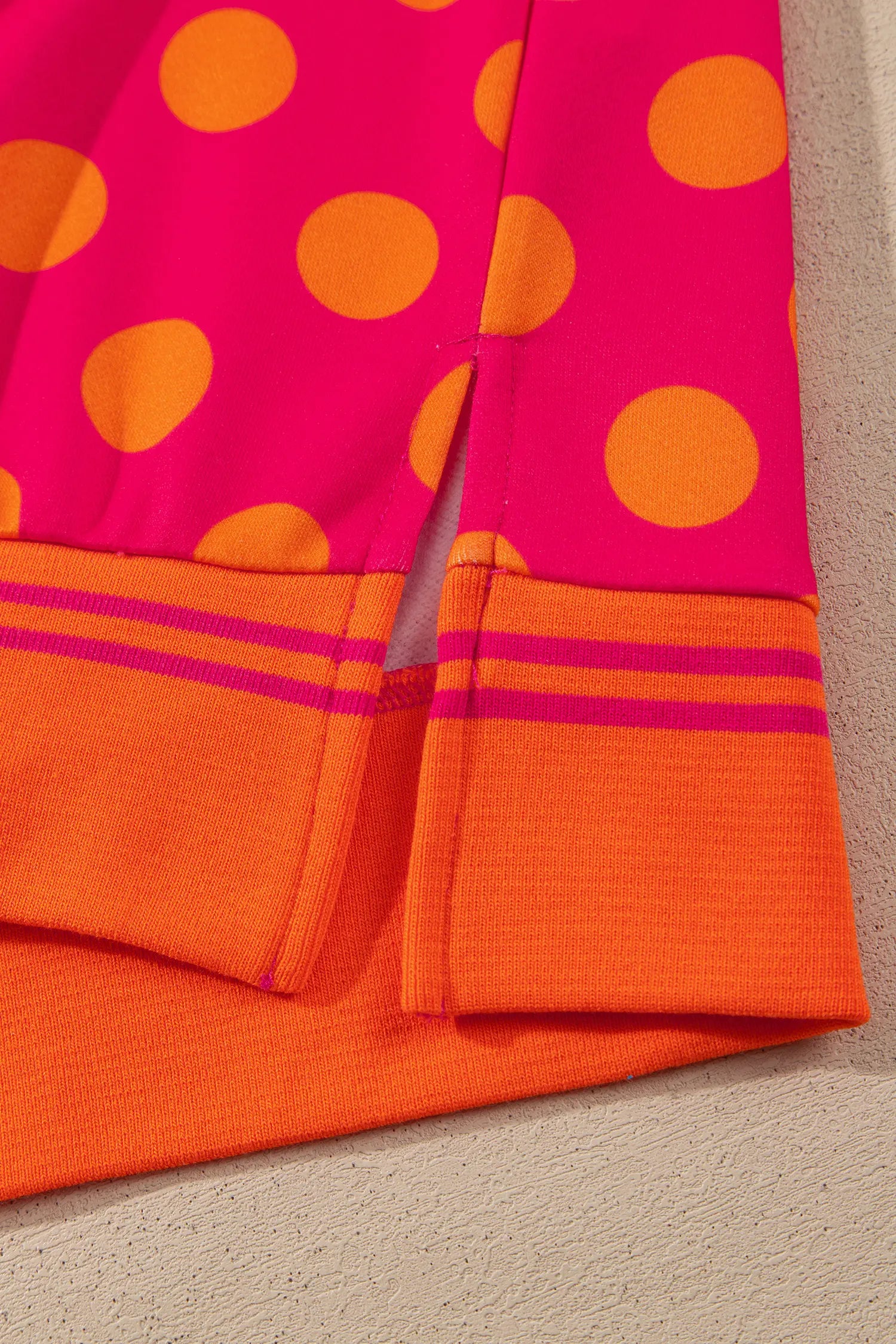 Close-up of striped hem band and side slit on rose polka dot sweatshirt