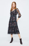 Woman wearing a dark floral dress with sheer sleeves on a white background