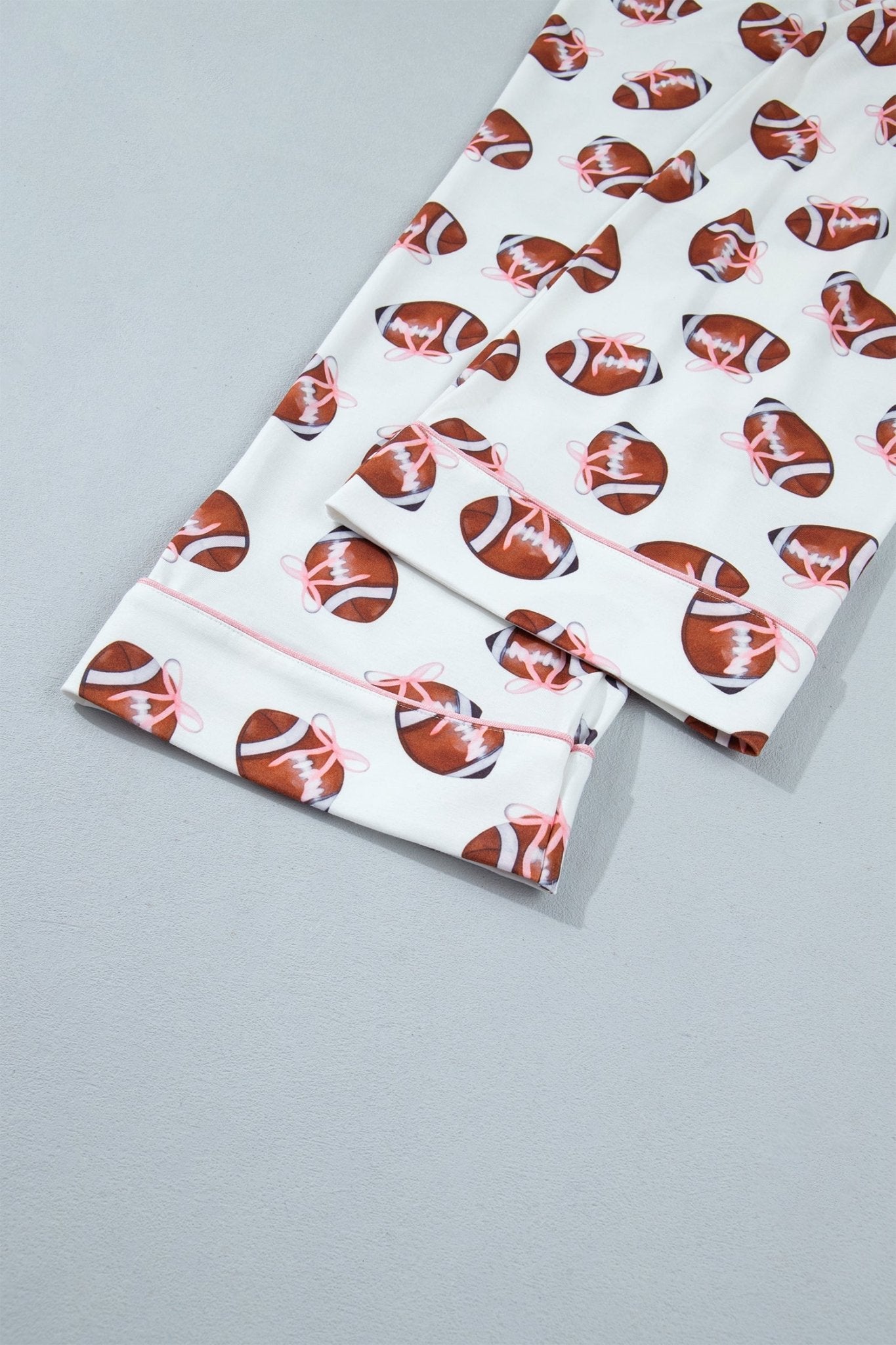 White pajama pants with an all-over football print in brown, orange, and white, featuring a pink piping detail along the collar.