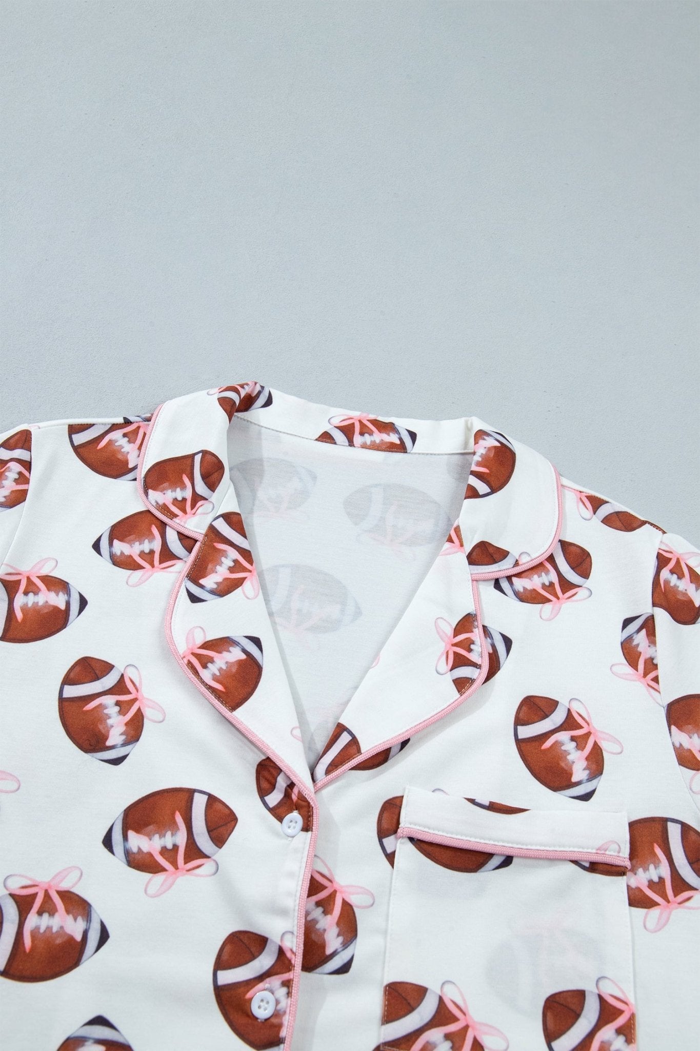 White pajama top with an all-over brown football print and pink piping along the collar, placket, and pocket.