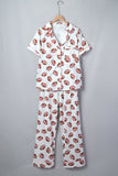 A two-piece short-sleeve pajama set hanging on a wooden hanger against a plain gray background. The pajama set features a white base fabric with an all-over print of brown and white footballs.