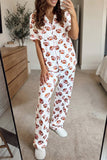 A woman takes a mirror selfie in a bedroom while wearing a white short-sleeve button-up pajama top and matching pajama pants, both covered in an allover brown football print. She is wearing white slippers.