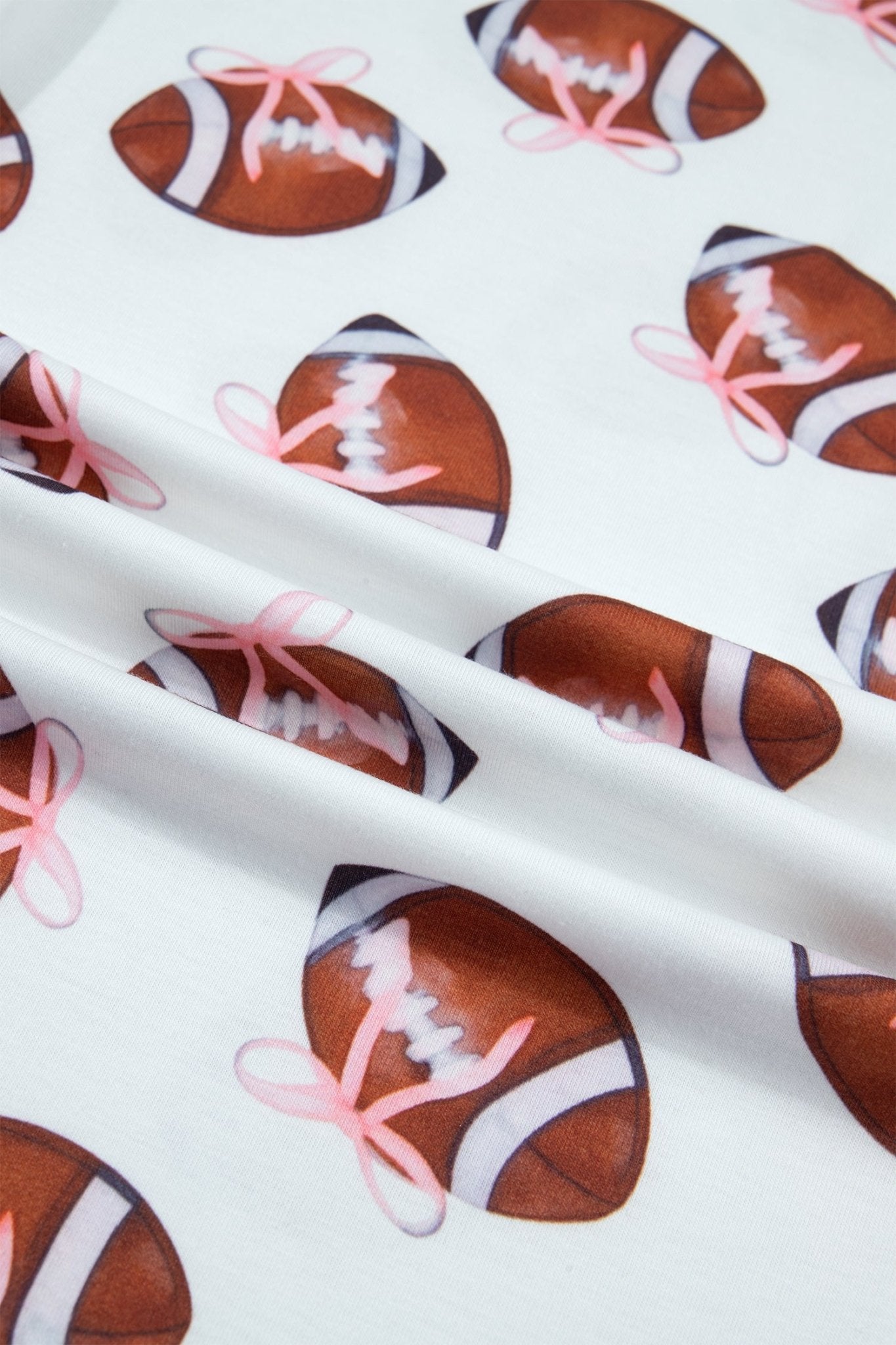 White fabric with a repeating pattern of brown footballs tied with pink bows, draped to show the material texture.