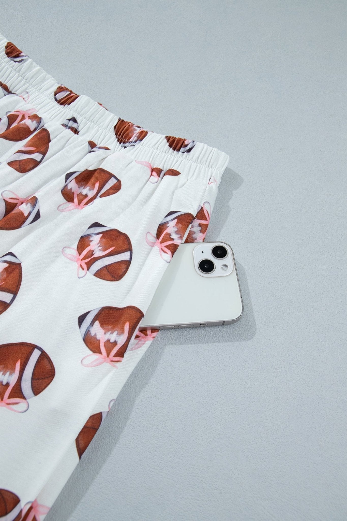 White boxer briefs with a brown and pink football print, shown next to a silver smartphone on a light gray background.