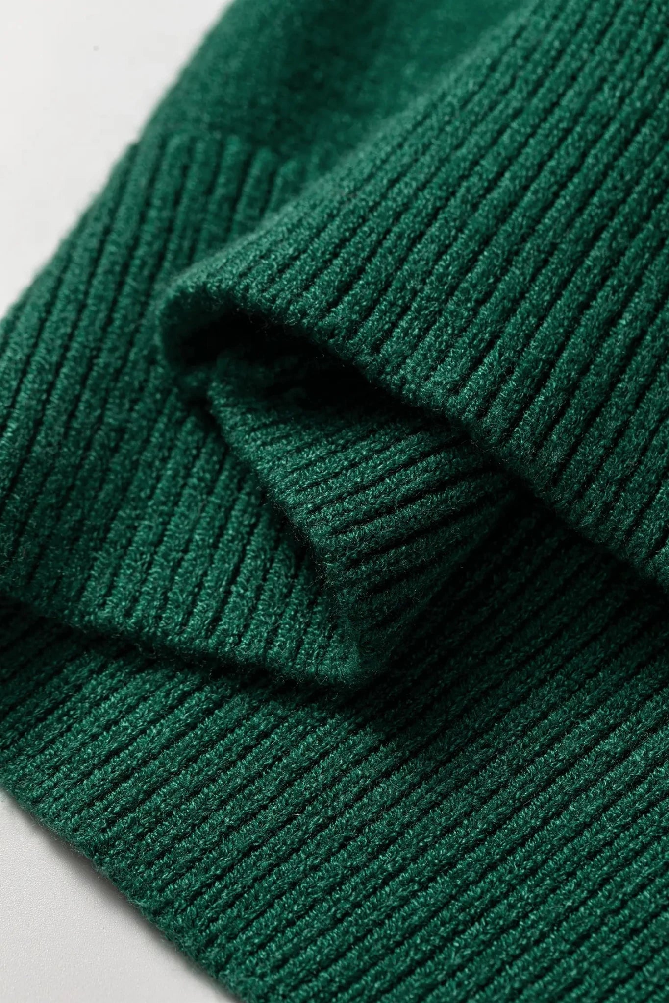 A close-up of a dark forest green ribbed knit fabric, showing the detailed texture and folds of the material.