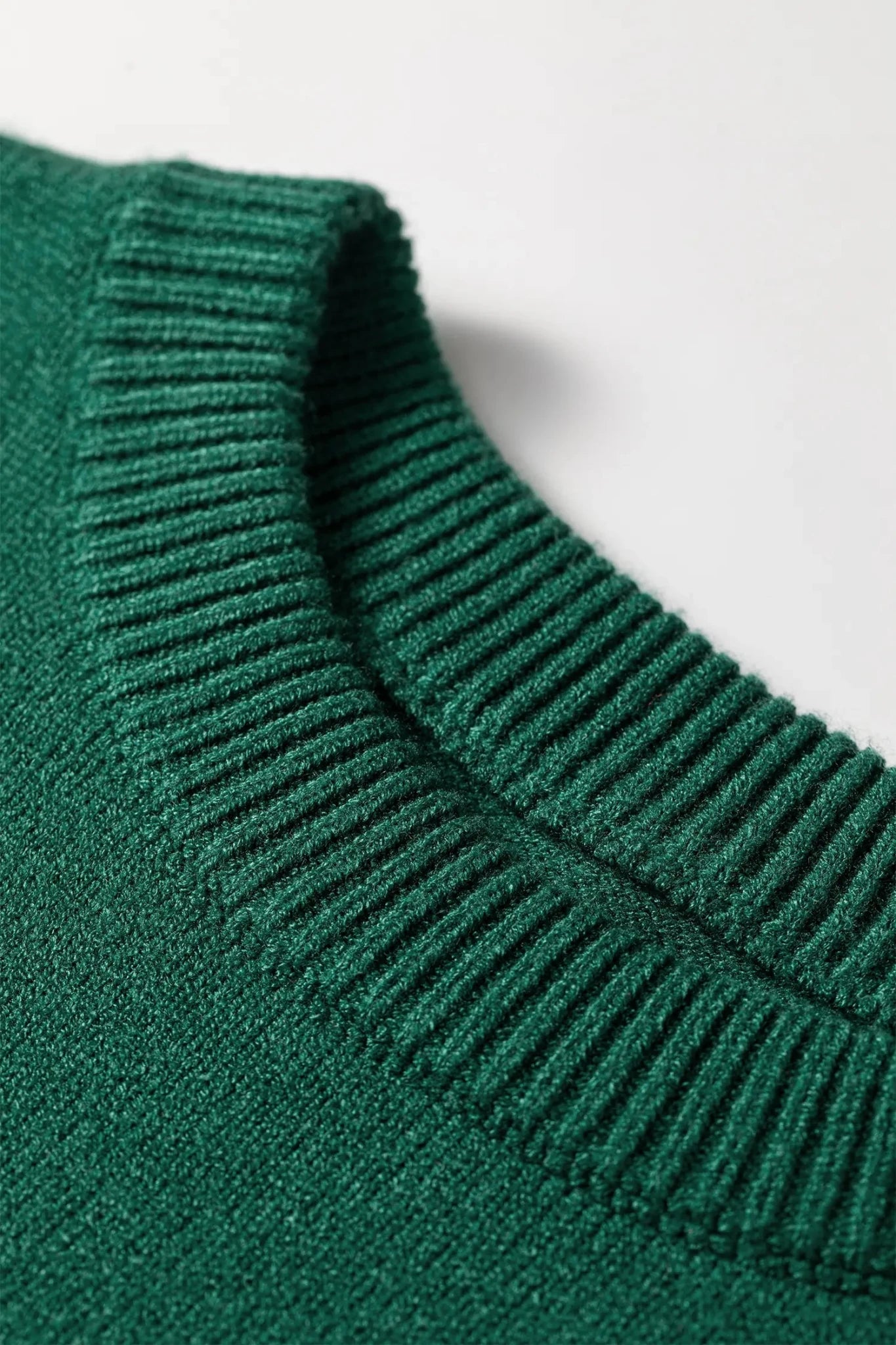 Close-up of a dark green ribbed knit sweater showing the crew neck collar against a light gray background.