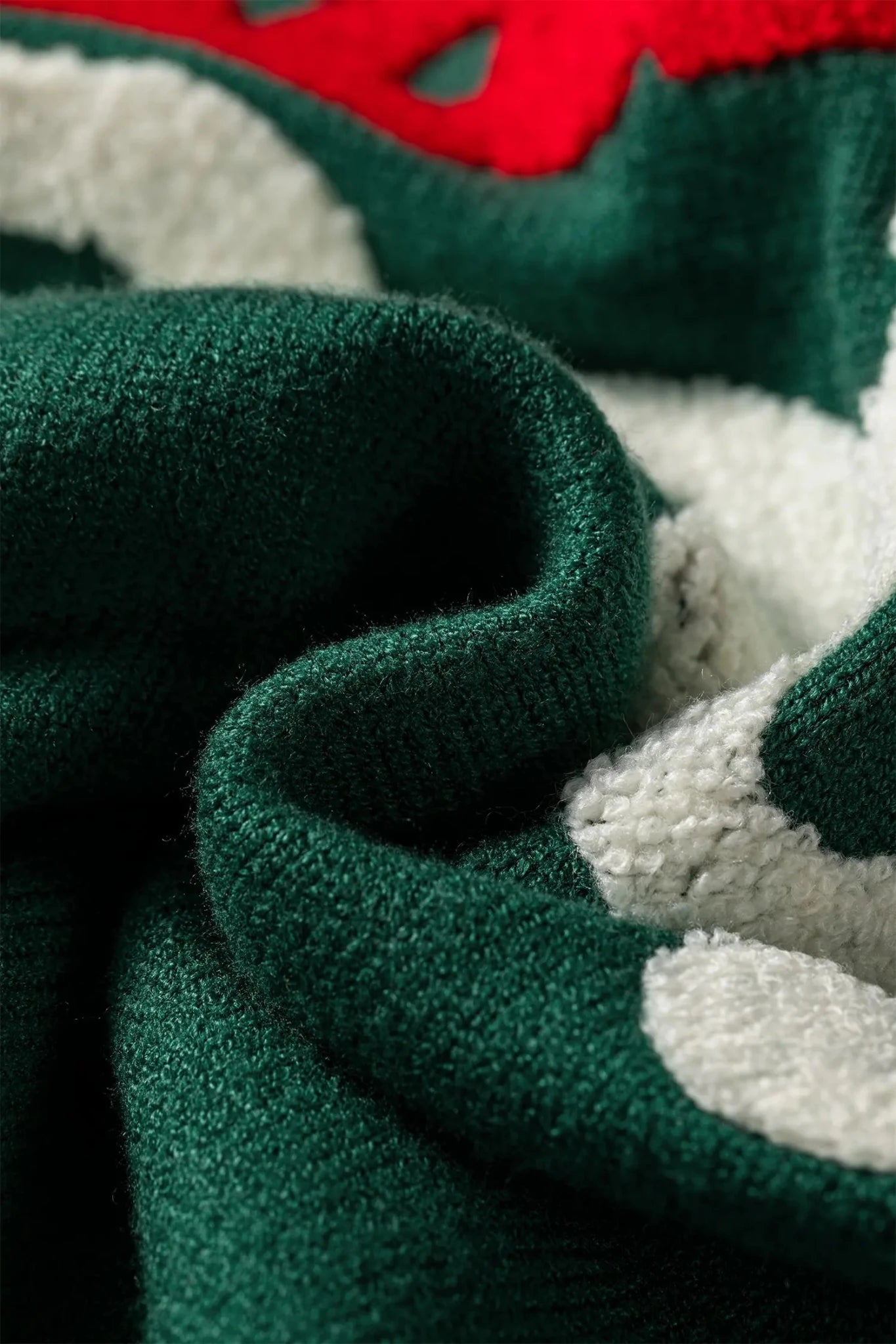 Close-up of a textured knit fabric with a holiday pattern, featuring dark green, white, and red sections.