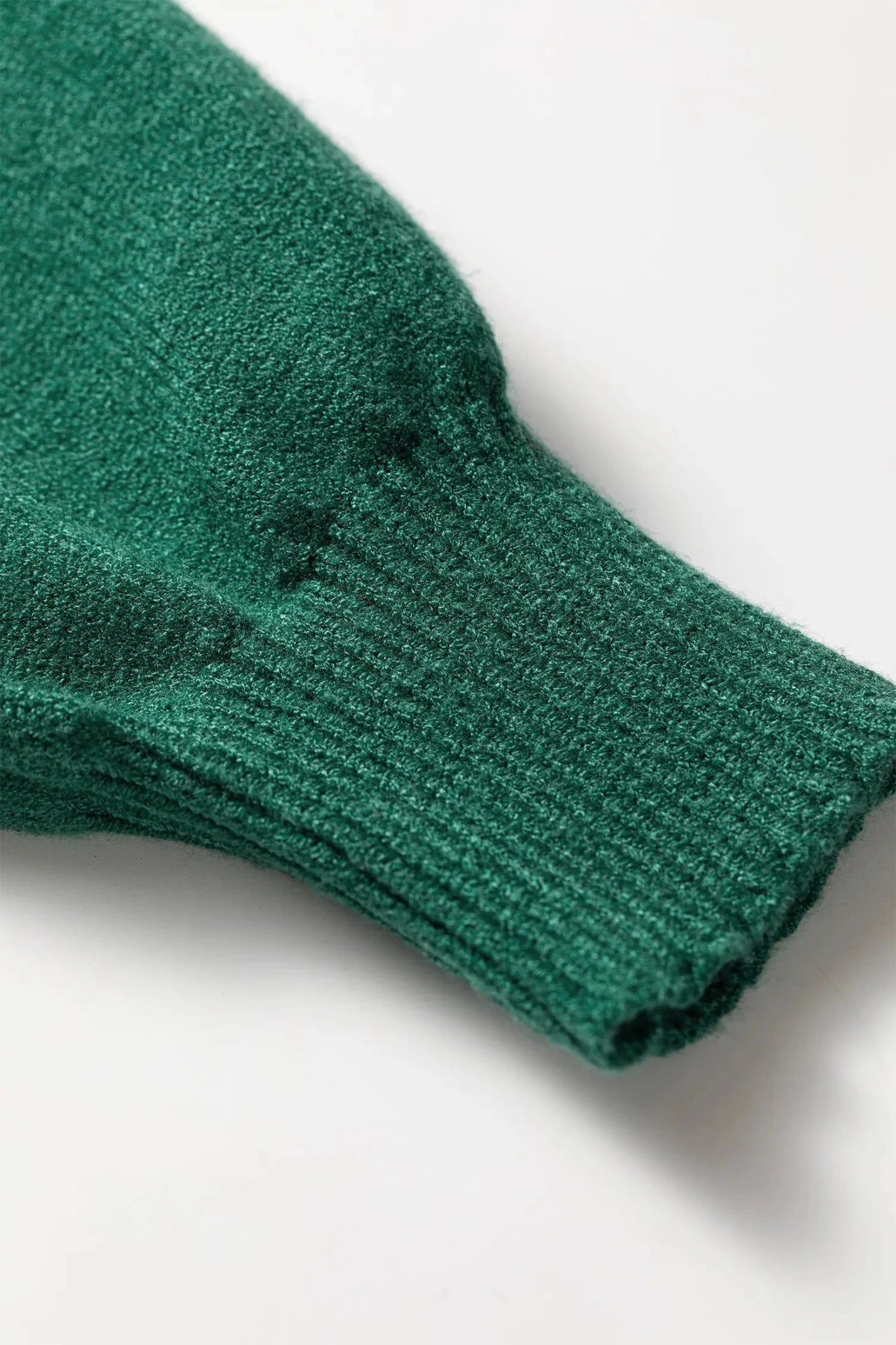 Close-up of a dark green ribbed knit sleeve or cuff on a white background.
