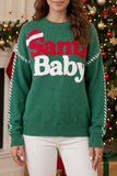 Woman wearing a green “Santa Baby” Christmas sweater in a festive room.