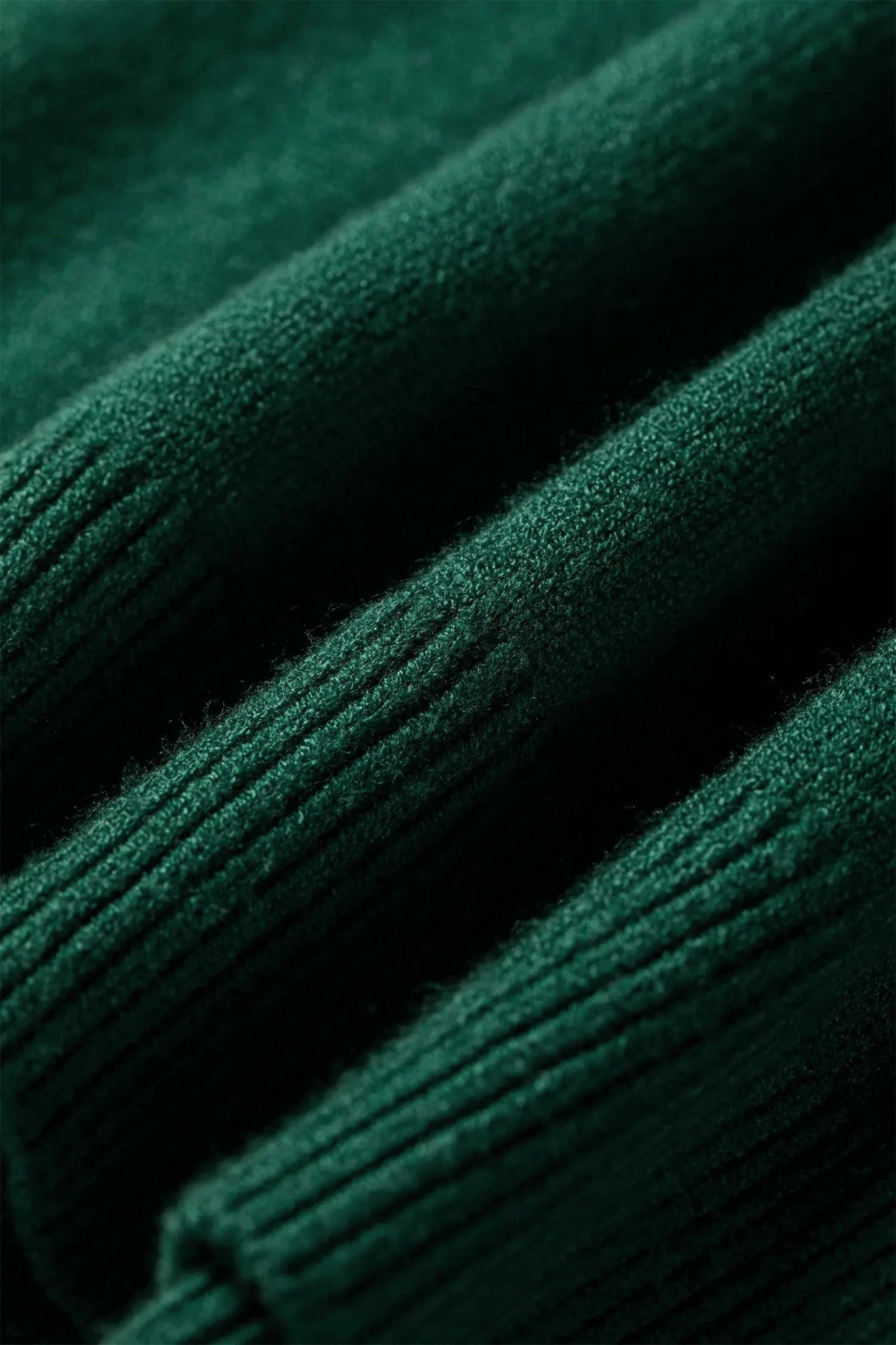 Close-up of dark forest green ribbed knit fabric texture with soft folds and fine yarn detail.