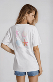Woman wearing a white t-shirt with colorful designs on the back against a plain background