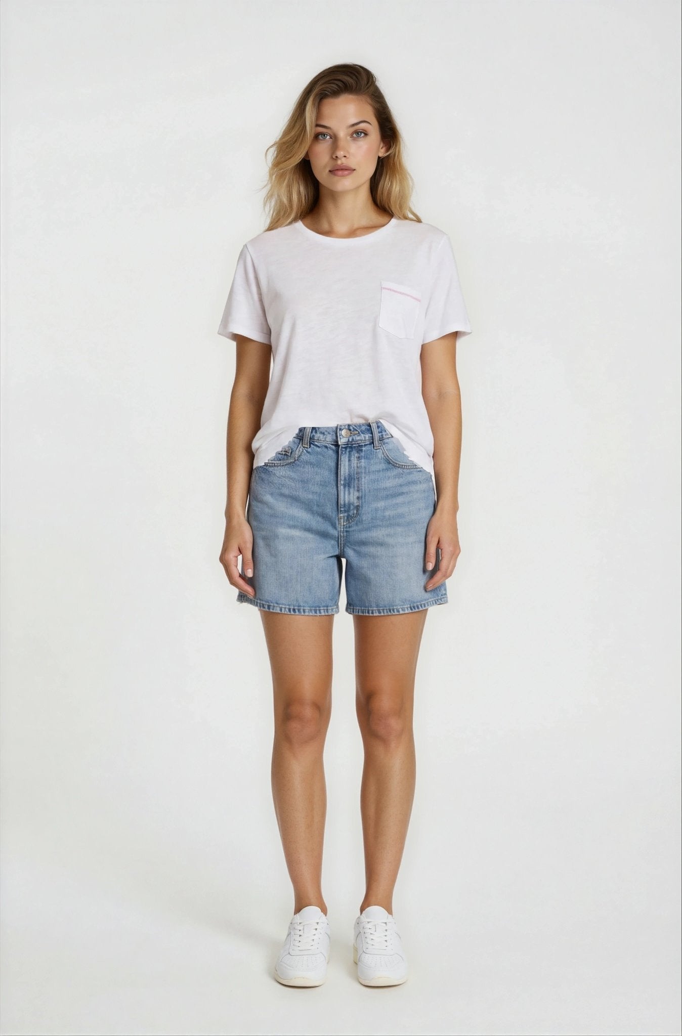 Woman wearing a white t-shirt and denim shorts on a plain background