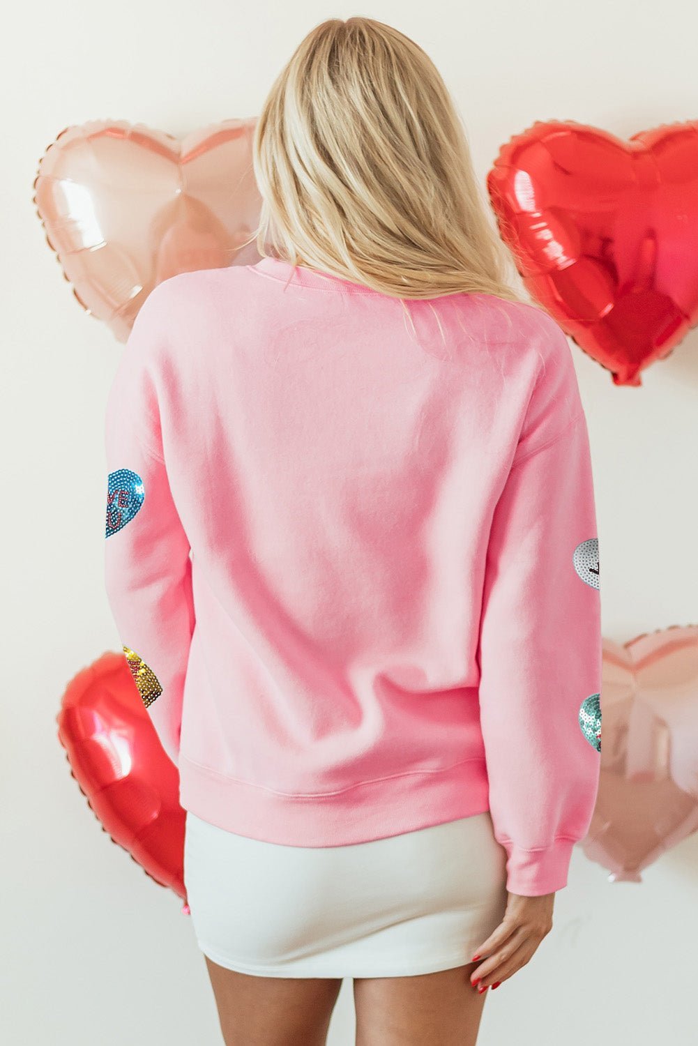 Person wearing a pink sweatshirt with heart designs in front of heart-shaped balloons.
