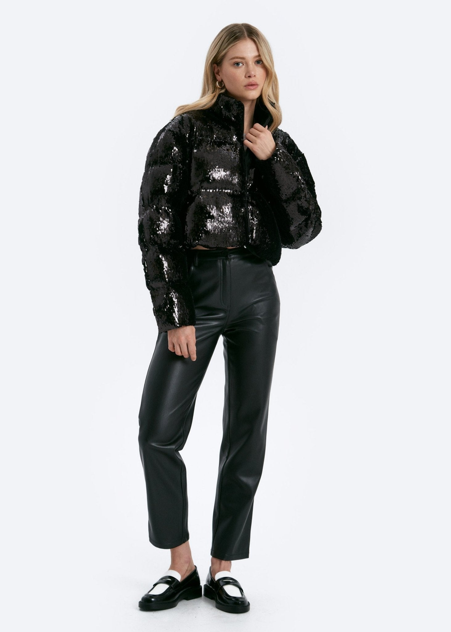 Woman wearing a black sequin jacket and black leather pants on a white background