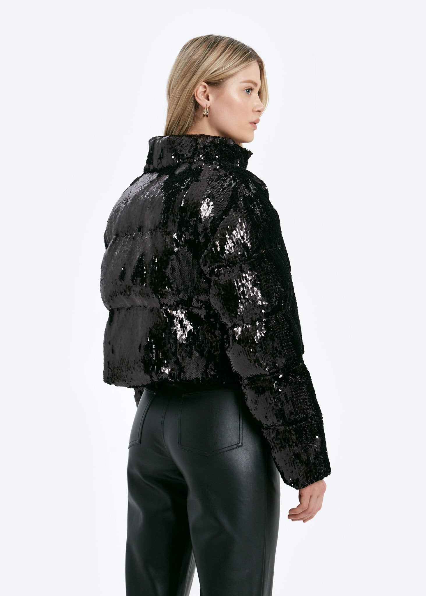 Person wearing a black sequin puffer jacket on a white background