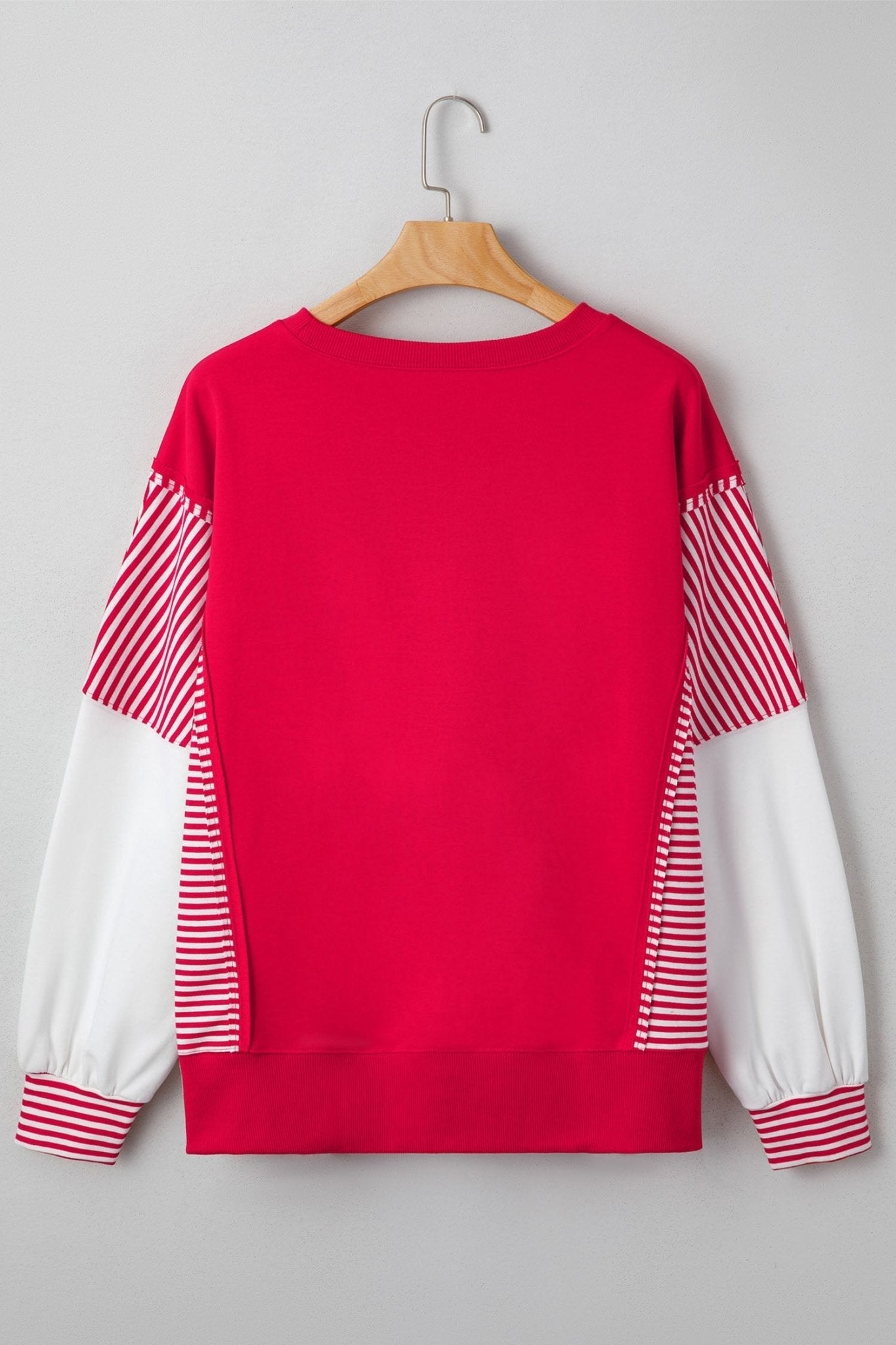 Red sweater with white and red striped sleeves on a hanger against a gray background