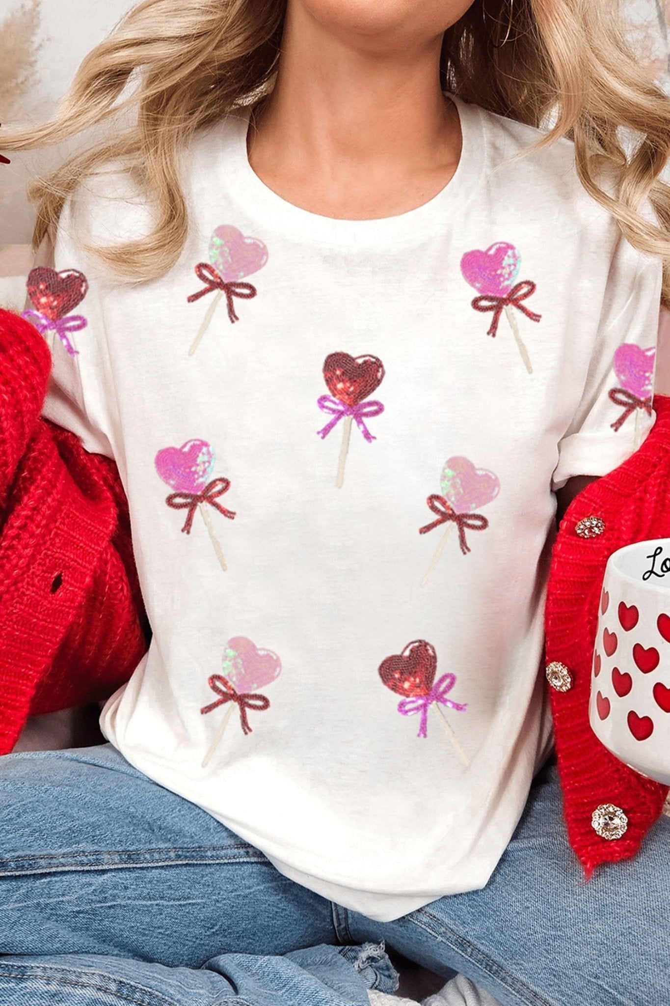 Person wearing a white shirt with heart and bow designs, sitting on a red chair.