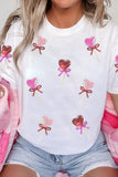 Person wearing a white t-shirt with heart and bow designs, sitting on pink fabric.
