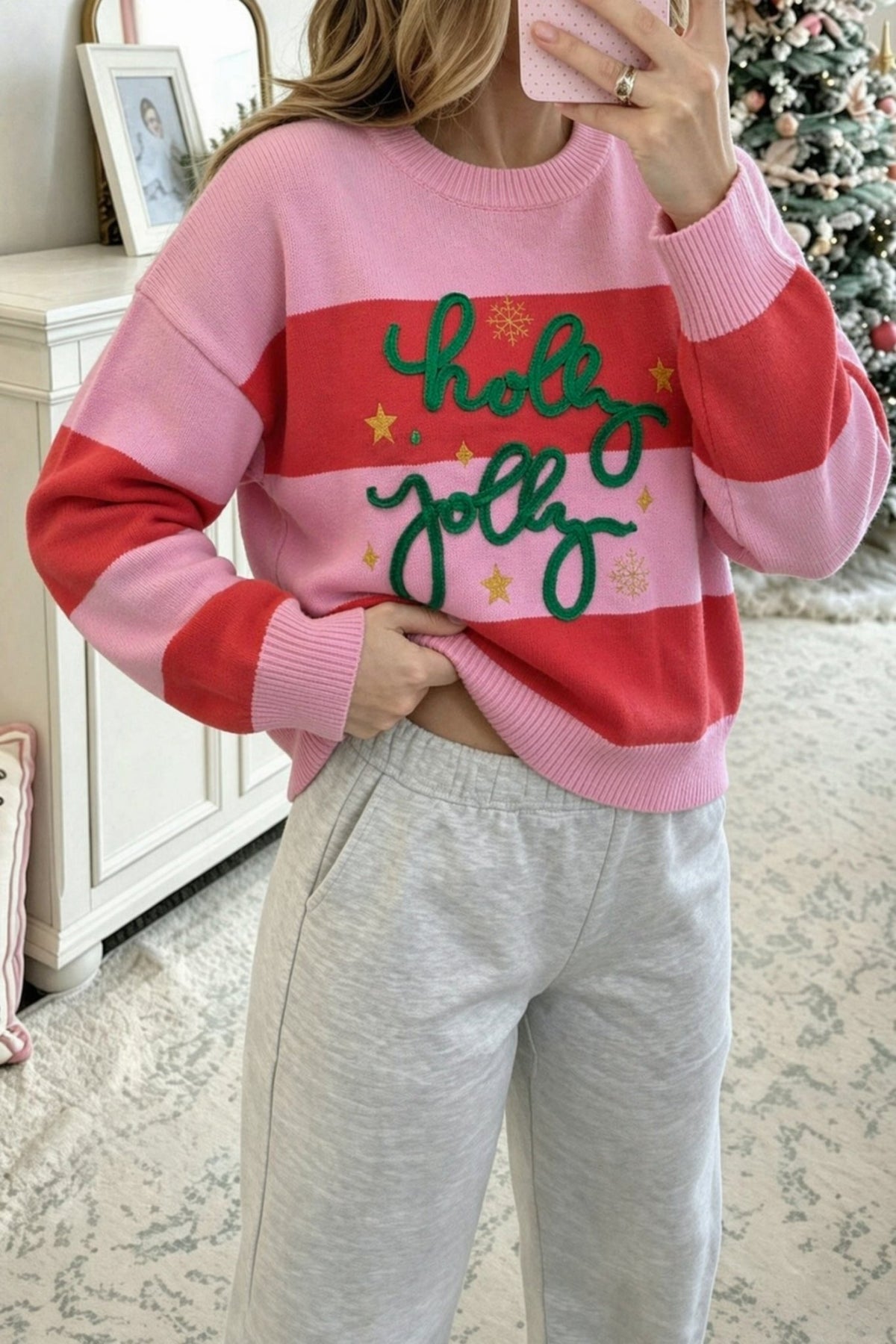 Woman in pink-red striped “holy jolly” sweater with gray sweatpants, mirror selfie.