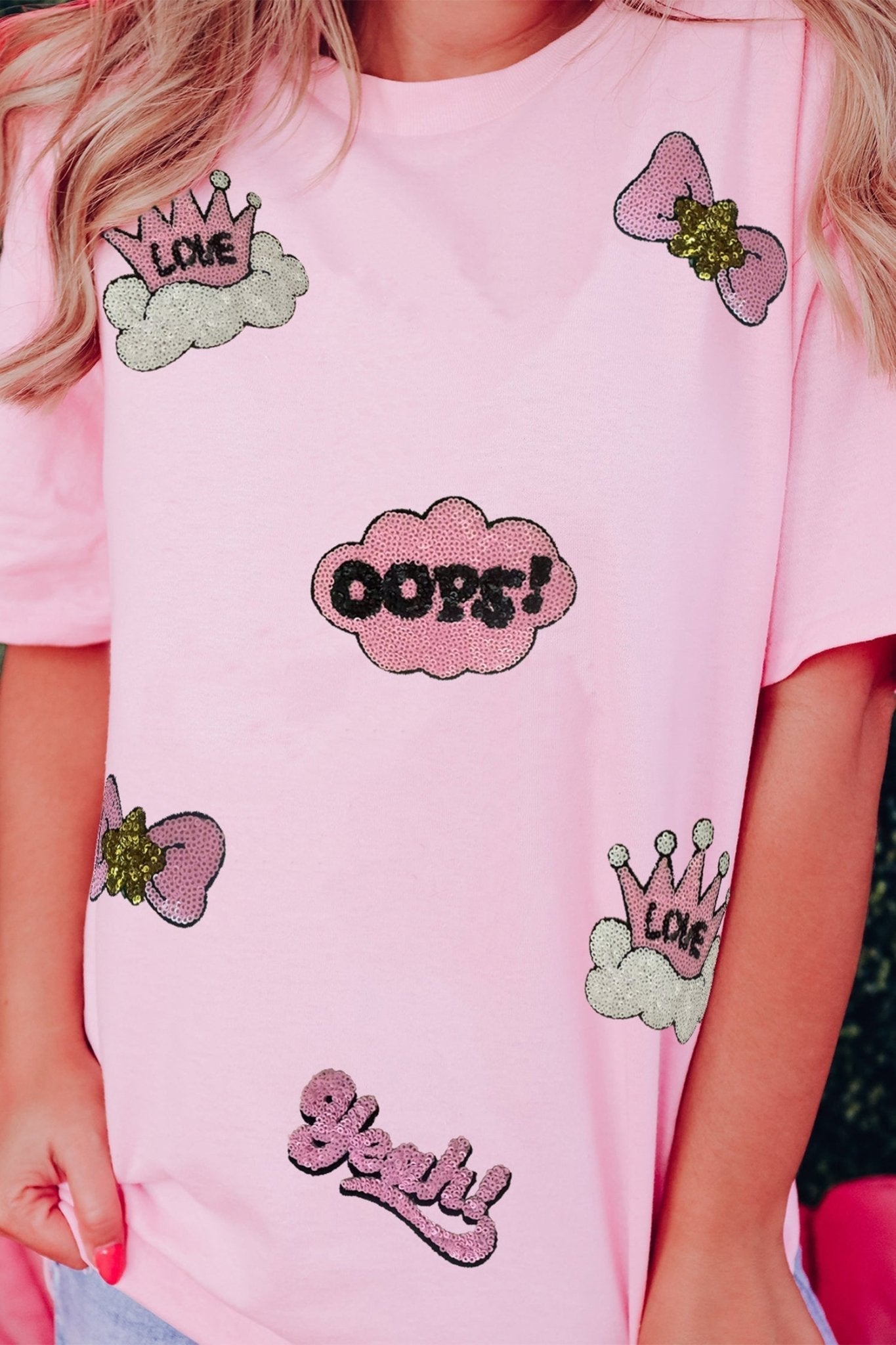 Pink t-shirt with various designs including hearts, crowns, and text on a person wearing it.