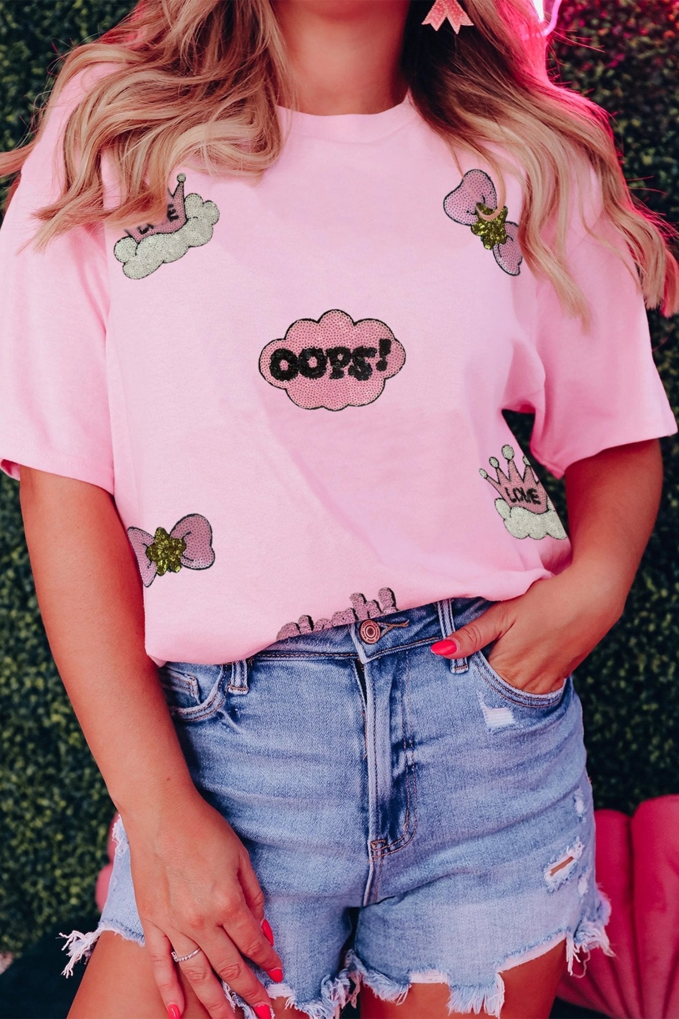 Person wearing a pink t-shirt with graphics and text, standing against a grassy background.