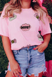 Person wearing a pink t-shirt with graphics and text, standing against a grassy background.