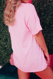 Person wearing a pink oversized t-shirt against a textured green wall.