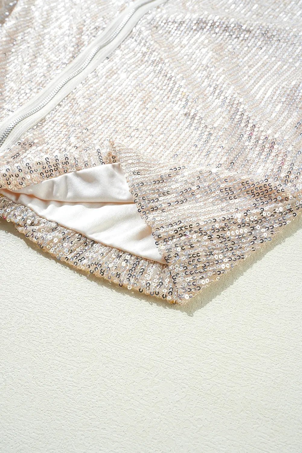 Close-up of champagne sequin garment with silver reflective sequins and white zipp