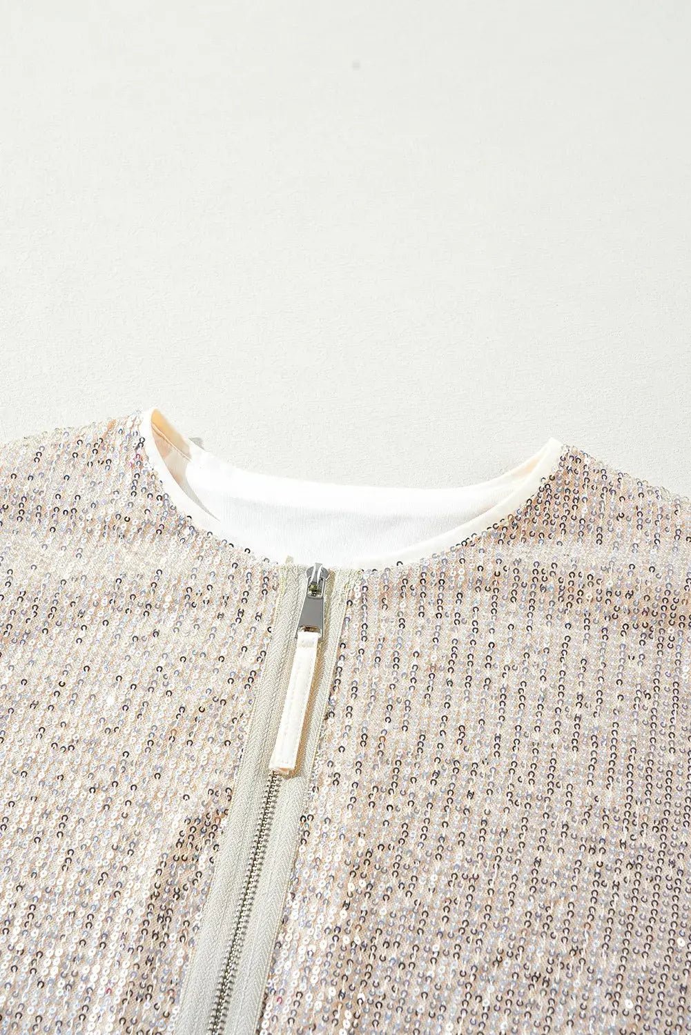 Close-up of beige-white speckled knit jacket with white collar and gold zipper pull.