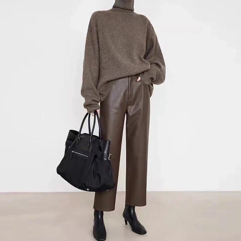 Person wearing a brown sweater and pants holding a black bag on a white background