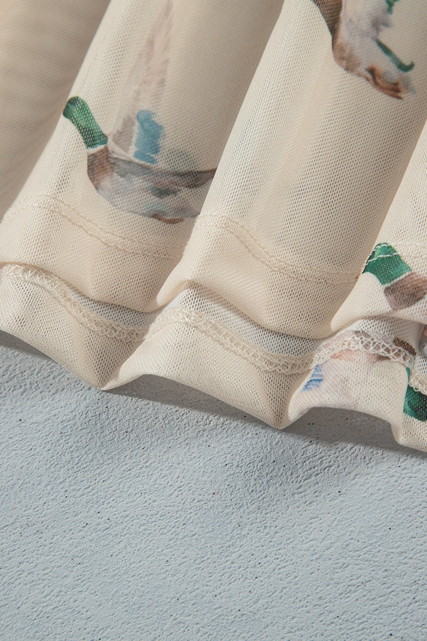 Close-up of a cream-colored curtain with a delicate bird pattern, draped over a textured light blue-gray wall.